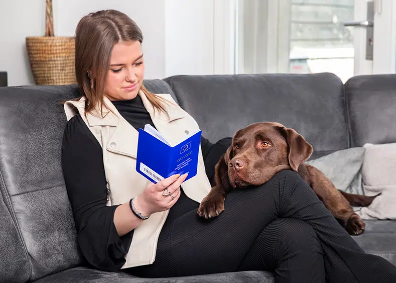 Vrouw bekijkt dierenpaspoort samen met bruine labrador op de bank