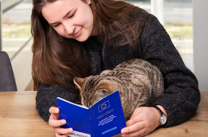 Vrouw toont dierenpaspoort aan kat tijdens controle op tafel