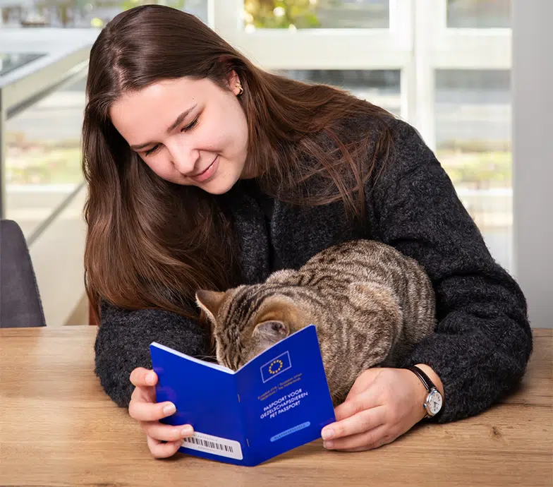Vrouw leest kattenpaspoort terwijl haar kat nieuwsgierig meekijkt op tafel