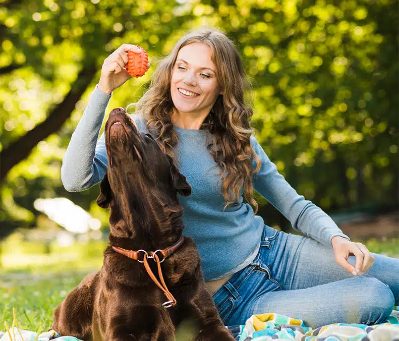 Blije vrouw speelt buiten met een bruine hond – minder stress door huisdier